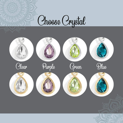 A jewelry color-options graphic titled 'Choose Crystal' showing six teardrop pendant charms in different crystal colors: Clear, Purple, Green, Blue, Clear with gold, and Purple with gold. Each pendant is displayed inside a white oval on a dark gray background with a light blue border.