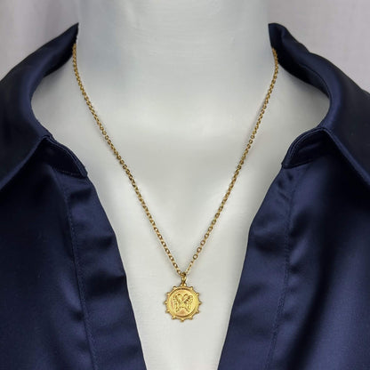 A gold chain necklace with a detailed medallion pendant displayed on a white mannequin torso wearing a navy blue satin shirt.