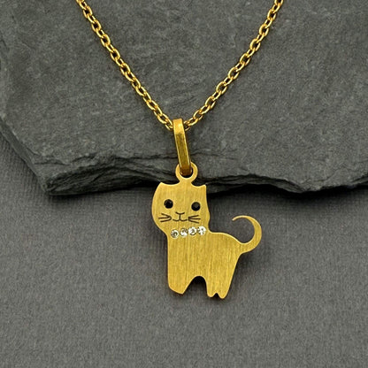 A gold cat-shaped pendant necklace with small clear rhinestones on its neck, displayed on a dark gray slate surface. 