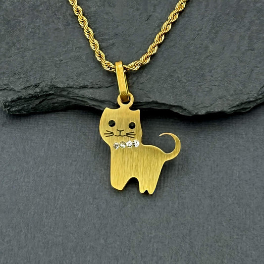 A gold cat-shaped pendant necklace with a small rhinestone detail on its chest, resting on a dark gray slate surface.