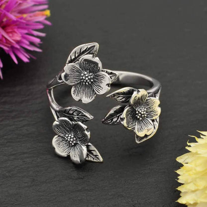 Close up of a floral adjustable sterling silver ring for women. Dogwood flowers meet at two ends of an open band.  There are three flowers with darker patina detail and leaves. 