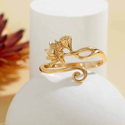 Close up of a shiny gold adjustable band ring with a lotus flower and louts bud on one side and a shiny gold swirl on the other. 