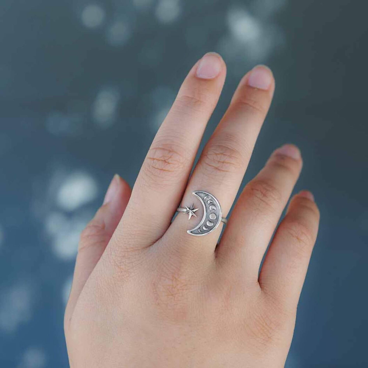 Hand model of a female with a half moon shaped silver end with moon phases and a star opposite. 