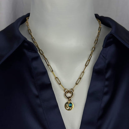 Gold paperclip chain necklace with a double-ring clasp and a small pendant featuring a blue-green stone, displayed on a white mannequin torso wearing a dark navy satin shirt.