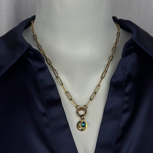 Gold paperclip chain necklace with a double-ring clasp and a small pendant featuring a blue-green stone, displayed on a white mannequin torso wearing a dark navy satin shirt.