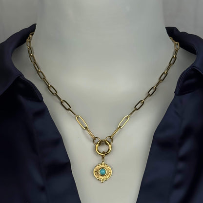 A gold paperclip chain necklace with a circular ring connector and a round gold pendant featuring a turquoise blue stone, displayed on a white mannequin bust wearing a dark navy satin shirt.